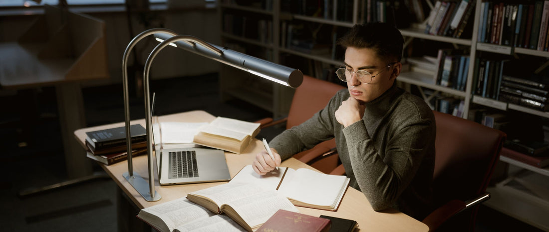 Adult private candidate revising with textbooks and a laptop at a library desk ahead of an A-Level resit